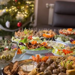 FIRA SP. Z O. O. - Stół zastawiony różnorodnymi przekąskami, w tym sałatki, roladki, klopsiki i smażone kąski, udekorowany warzywami i wykałaczkami, z choinką w tle.