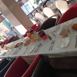 FIRA SP. Z O. O. - Długi stół z białym obrusem, nakryty zastawą, napojami i przekąskami, przygotowany dla gości; widoczne krzesła w kolorach czerwonym i czarnym.