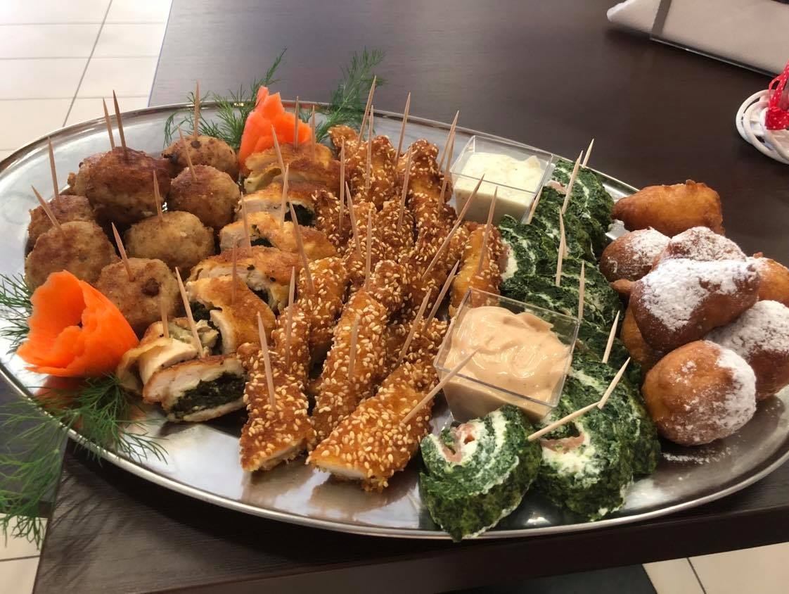 Srebrna patera z różnorodnymi przekąskami: kotleciki, roladki z farszem szpinakowym, paluszki w sezamie, pączki z cukrem pudrem, sosy w przezroczystych pojemnikach, udekorowane koperkiem i rzeźbą...