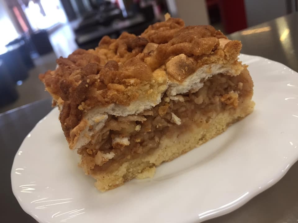 Kawałek domowej szarlotki z kruszonką na białym talerzu, widoczne jabłkowe nadzienie i kruche ciasto.