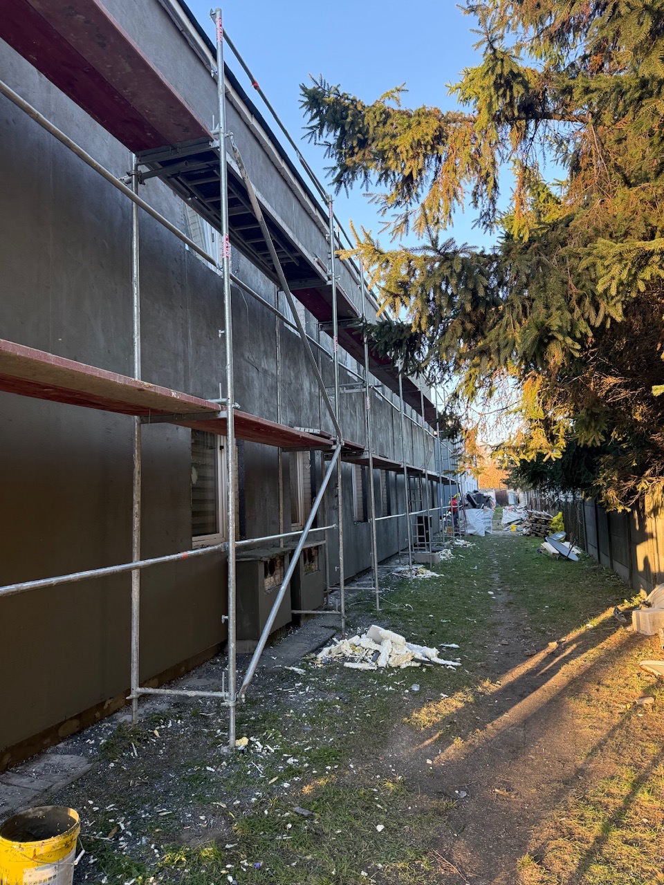 Elewacja budynku w trakcie prac w Przasnyszu. Widoczne rusztowania, ocieplenie i fragmenty styropianu. Świeżo nałożony tynk w kolorze szarym.