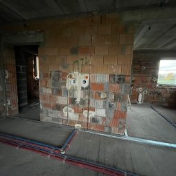 ElektroTechInstal Patryk Kowalczyk - Surowy stan instalacji elektrycznej w budynku: przewody w ścianie z cegły dziurawki, rury w podłodze, widoczne puszki instalacyjne. Wnętrze w trakcie budowy.