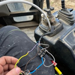 ElektroTechInstal Patryk Kowalczyk - Elektryk łączy przewody wewnątrz kabiny maszyny budowlanej. Widoczne złącza, przewody w różnych kolorach i narzędzia. Praca w trudnych warunkach.