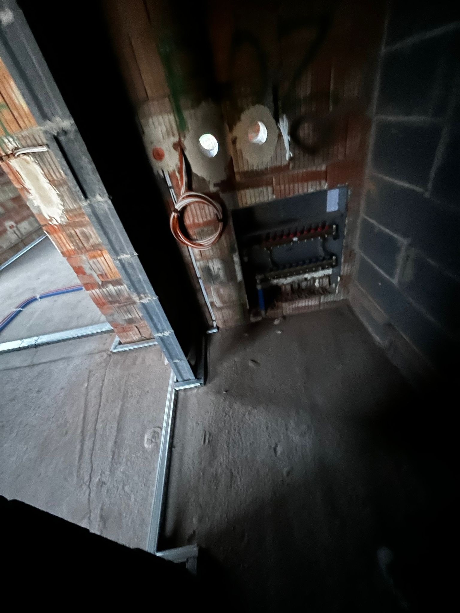 Wnętrze w trakcie prac instalacyjnych: widoczne przewody elektryczne, rozdzielnica i elementy konstrukcyjne sufitu podwieszanego. Surowy stan, cegła i beton.