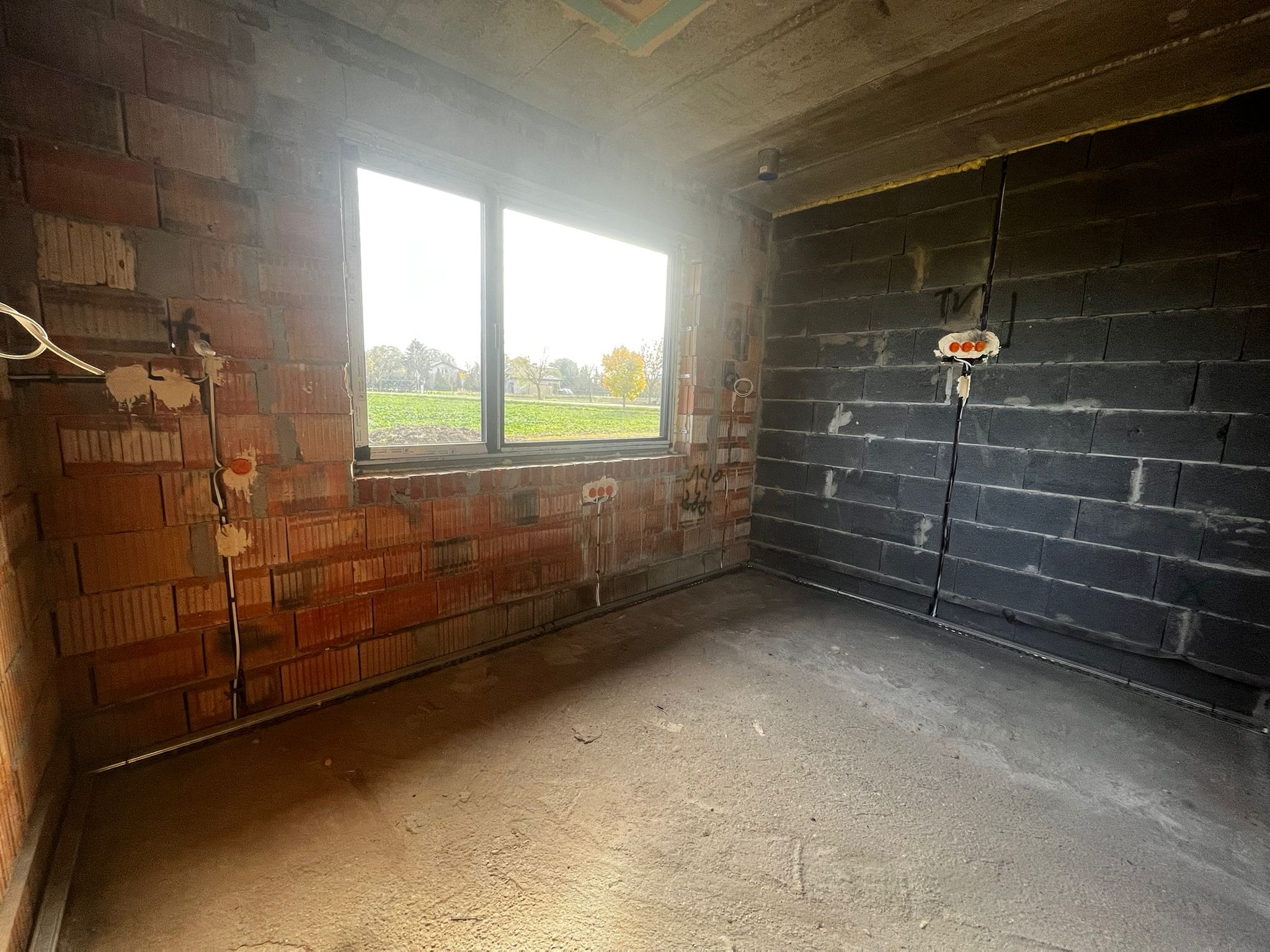 Surowy stan: instalacja elektryczna w nowym budynku z czerwonej cegły i szarego betonu komórkowego. Widoczne kable i puszki elektryczne przed tynkowaniem.