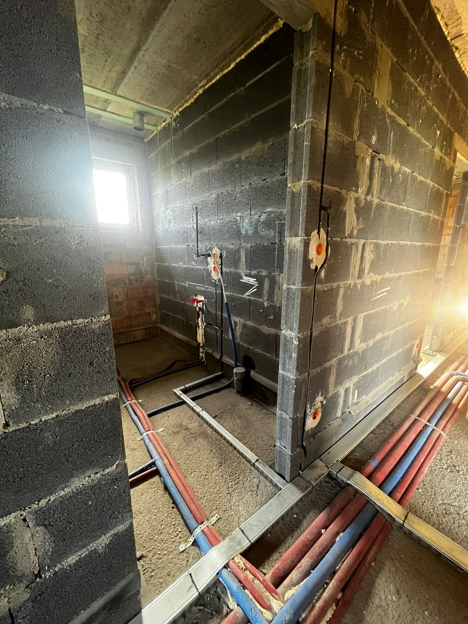 Surowy stan: Instalacja wodno-kanalizacyjna i elektryczna w bloku z betonu komórkowego. Widoczne rury, kable i puszki instalacyjne przed tynkowaniem. Oświetlenie naturalne.