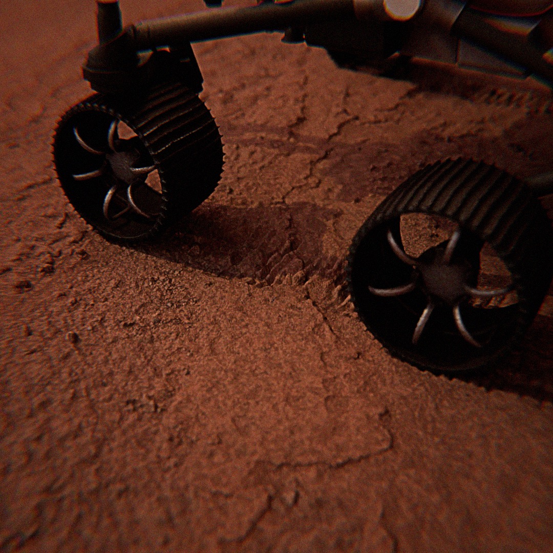 Nisko ustawiony model łazika marsjańskiego z widocznymi kołami na czerwonym, piaszczystym podłożu, sugerujący powierzchnię Marsa.