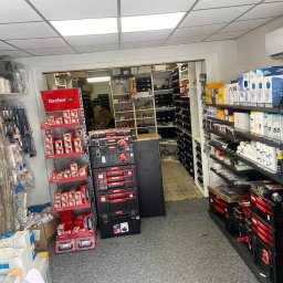 Sklep Instalacyjny hydrauliczny Poznań - Doradca Energetyczny - pompy ciepła - kotły gazowe Poznań - Wnętrze sklepu z artykułami hydraulicznymi, widoczne regały z rurami, złączkami, narzędziami i skrzynkami narzędziowymi firmy Fischer, oświetlone lampami sufitowymi.