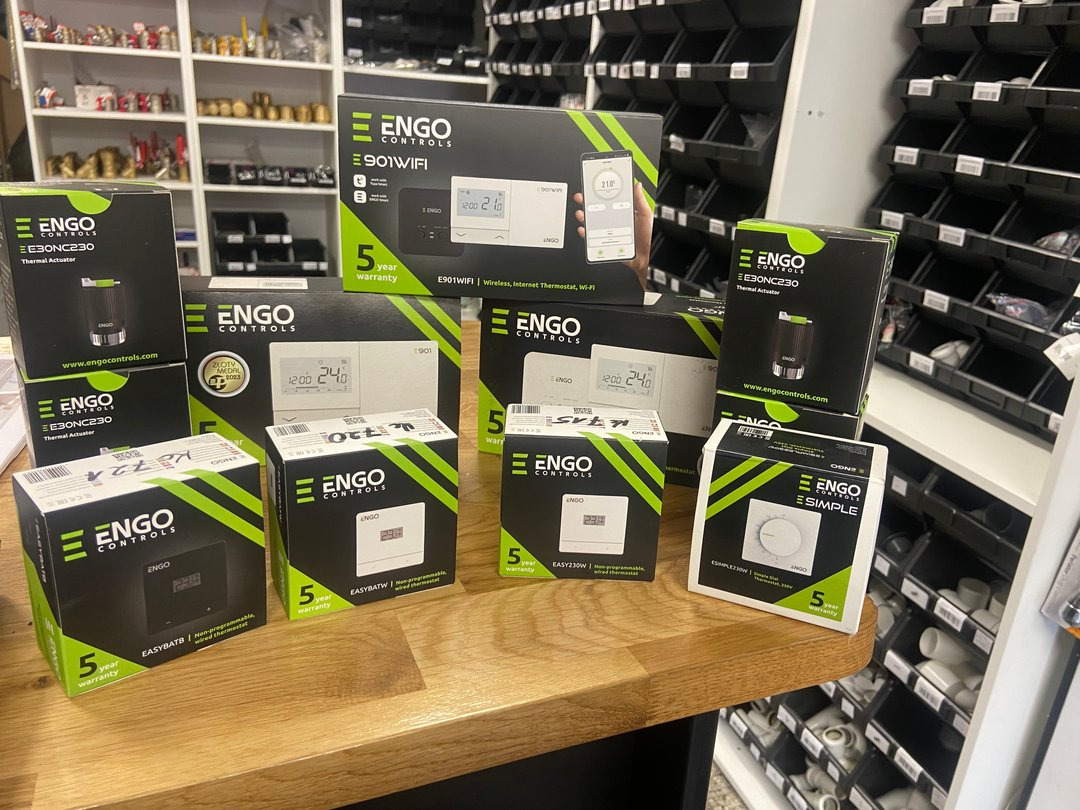 Ekspozycja różnorodnych termostatów i siłowników termicznych marki ENGO Controls w oryginalnych opakowaniach, z widocznym logo i oznaczeniem 5-letniej gwarancji, na drewnianym blacie sklepowym...