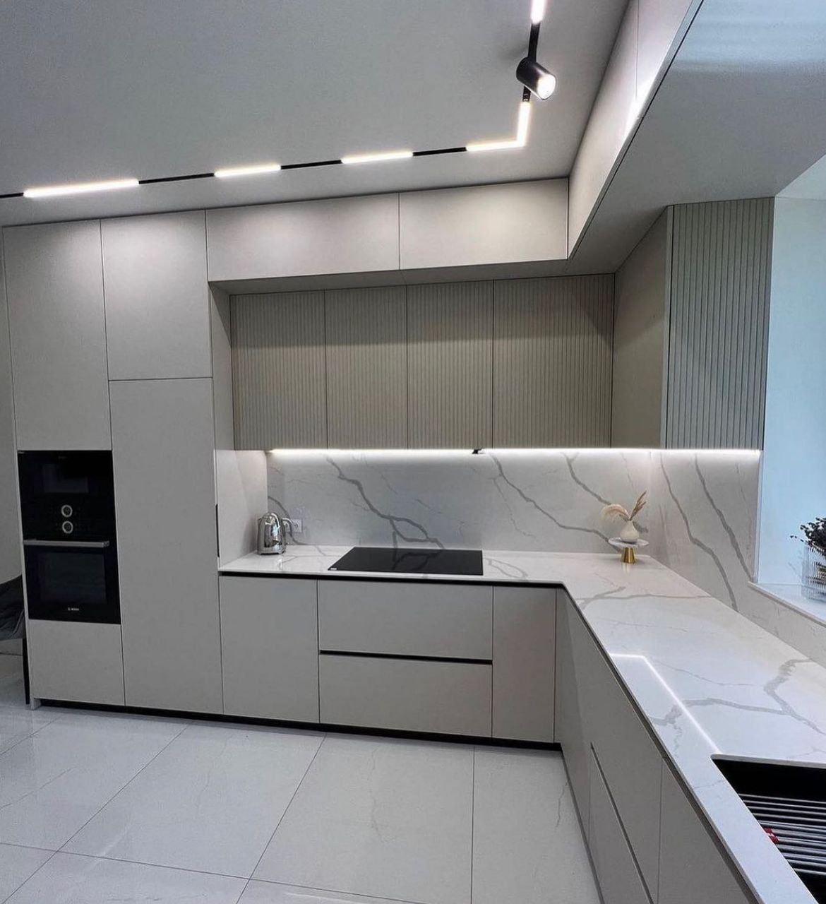 Nowoczesna kuchnia z szarymi frontami, blatem imitującym marmur, oświetleniem LED podszafkowym i punktowym na suficie.