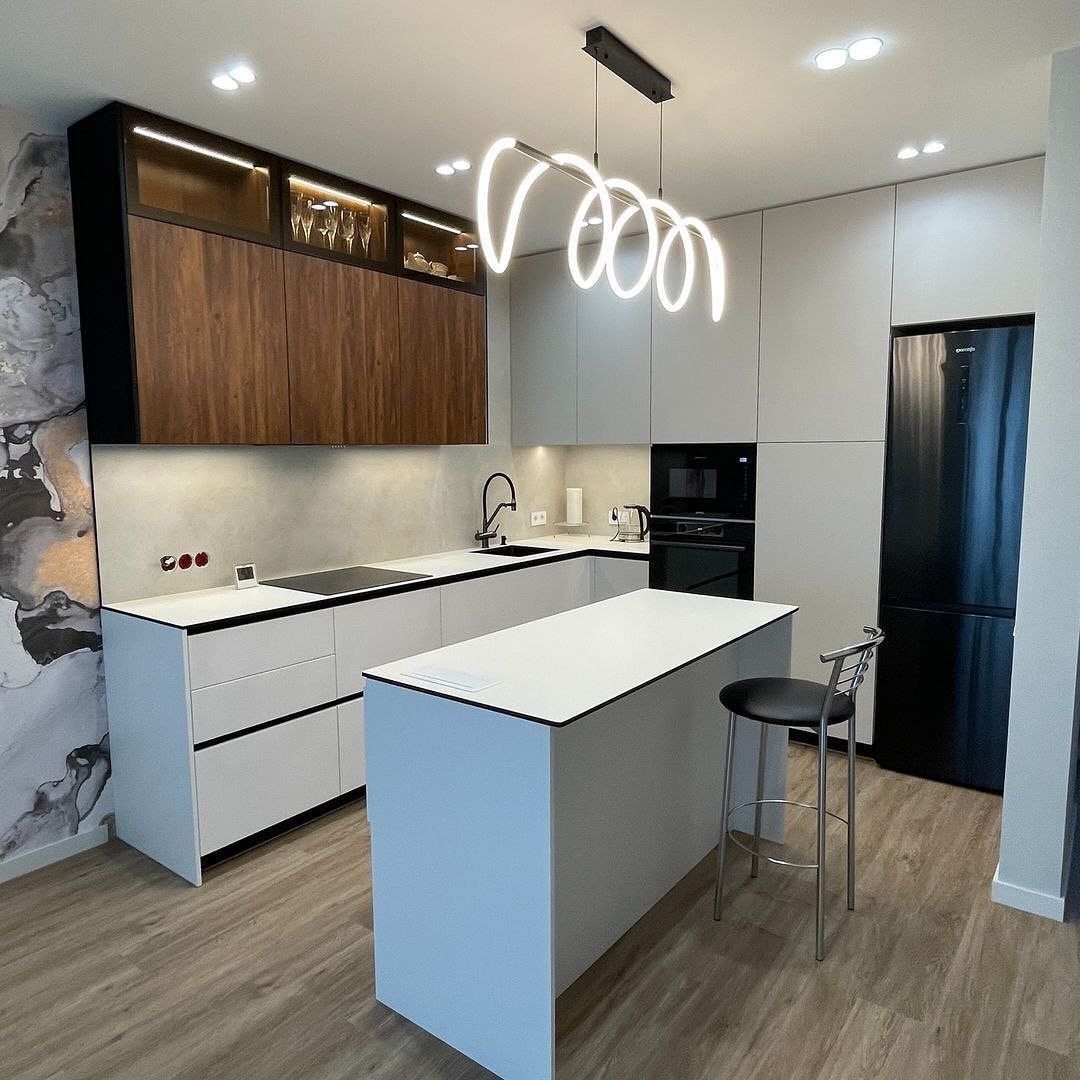 Nowoczesna kuchnia z wyspą w Warszawie, charakteryzująca się minimalistycznym designem, białymi frontami szafek z czarnymi obramowaniami, drewnianymi szafkami wiszącymi z podświetleniem...