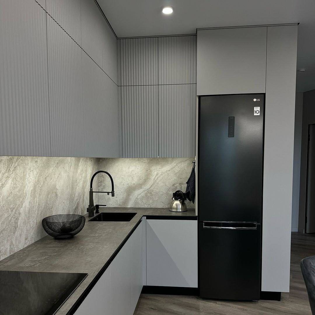 Nowoczesna kuchnia w szarościach z frezowanymi frontami szafek górnych, czarnym zlewem i baterią oraz czarną lodówką LG.