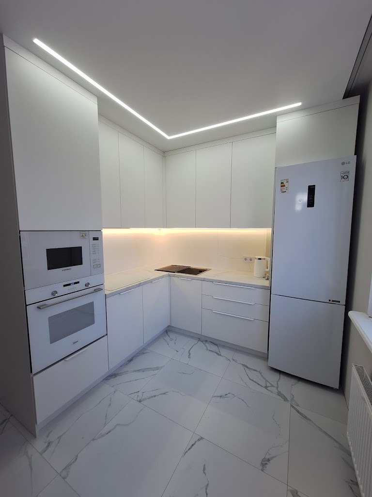 Biała, minimalistyczna kuchnia na wymiar z oświetleniem LED podszafkowym i sufitowym, marmurowa podłoga, zabudowany piekarnik i lodówka LG.