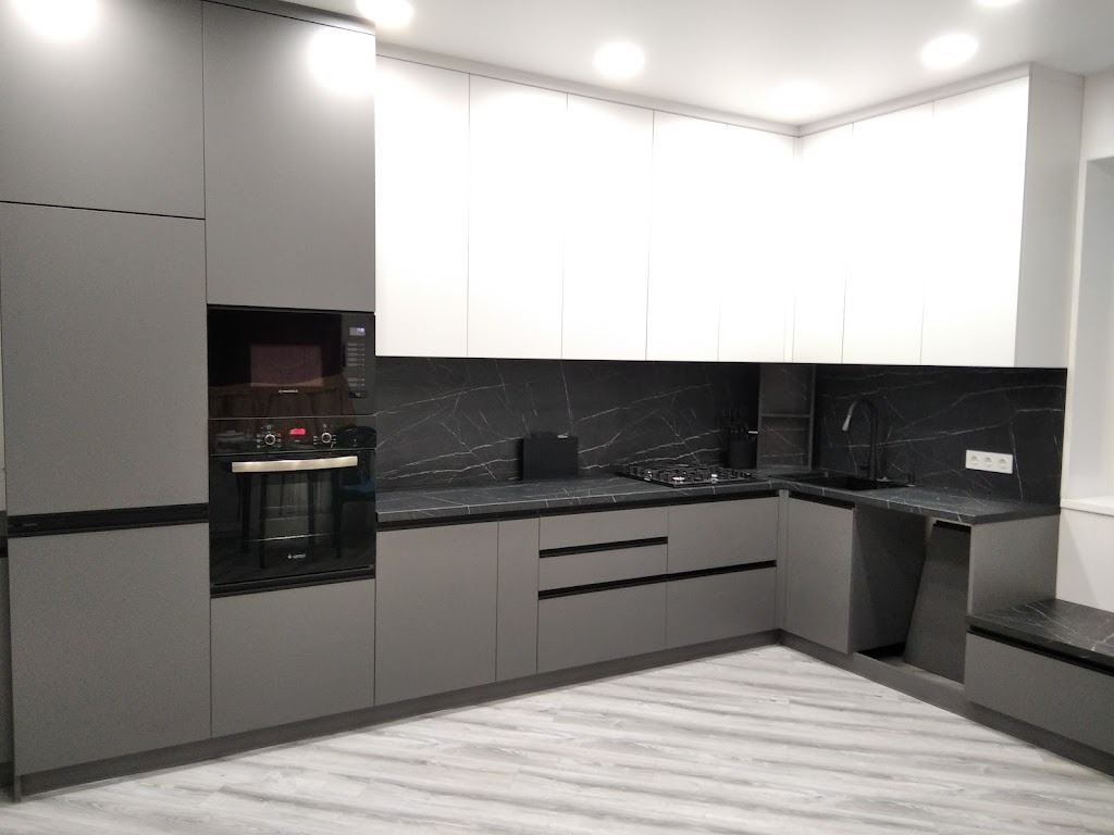 Nowoczesna kuchnia z szarymi szafkami dolnymi i białymi górnymi, czarny blat z marmurowym wzorem, płyta gazowa i piekarnik w zabudowie.