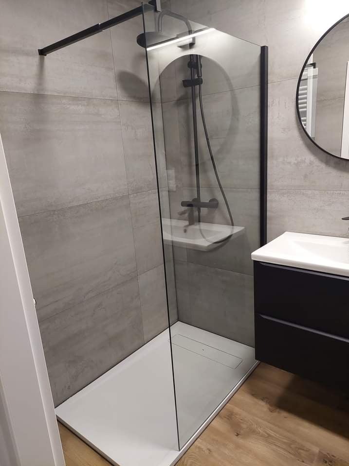 Nowoczesna kabina prysznicowa typu walk-in z czarnymi elementami armatury i szklaną ścianą, zamontowana w łazience w Wałbrzychu z szarymi płytkami imitującymi beton i drewnopodobną podłogą.