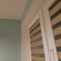 Mal-masters - Turkusowa ściana pomalowana w rogu pokoju, obok okno z beżowo-szarymi roletami w białem ramie.