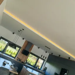 Nowoczesna kuchnia z wyspą, oświetleniem LED podsufitowym i wiszącymi lampami, widok z dołu, okna z widokiem na ogród.