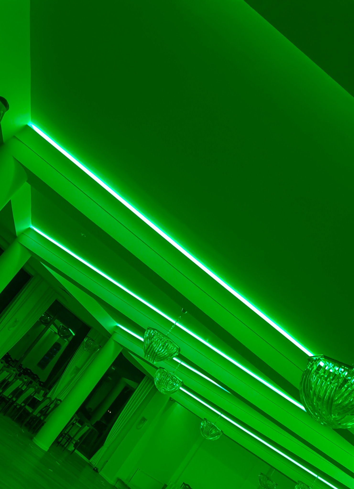 Wnętrze sali balowej z zielonym oświetleniem LED w listwach sufitowych i ozdobnymi, szklanymi żyrandolami.