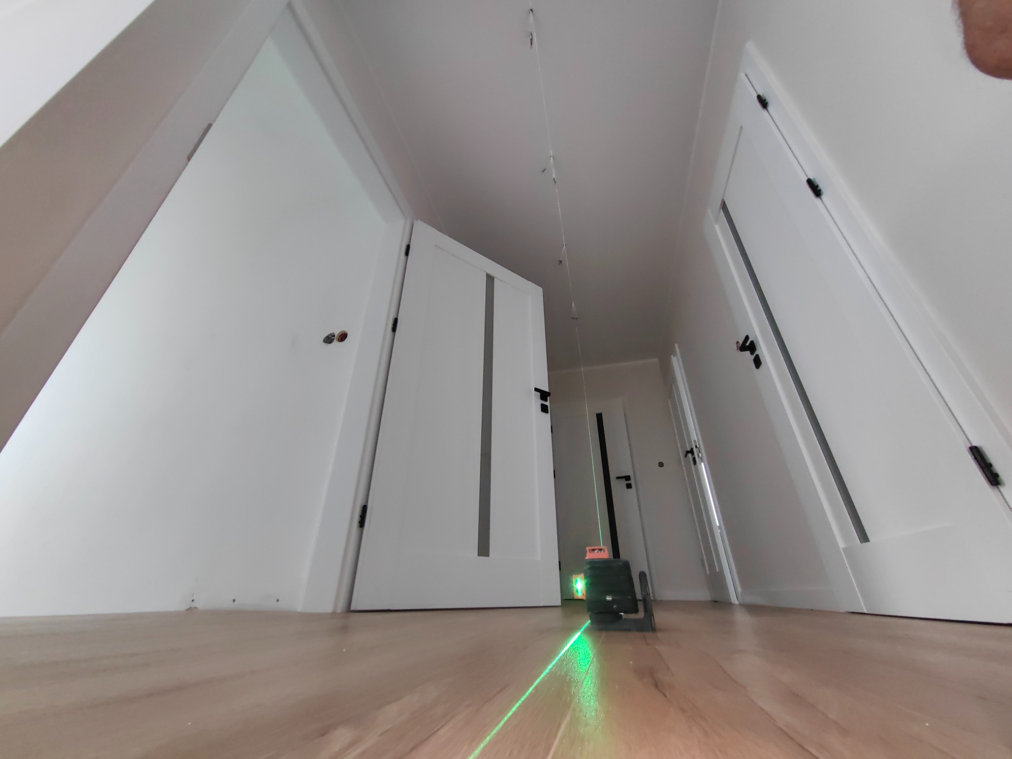 Laser krzyżowy emituje zielone linie na podłodze podczas poziomowania w pomieszczeniu z białymi drzwiami i listwami.