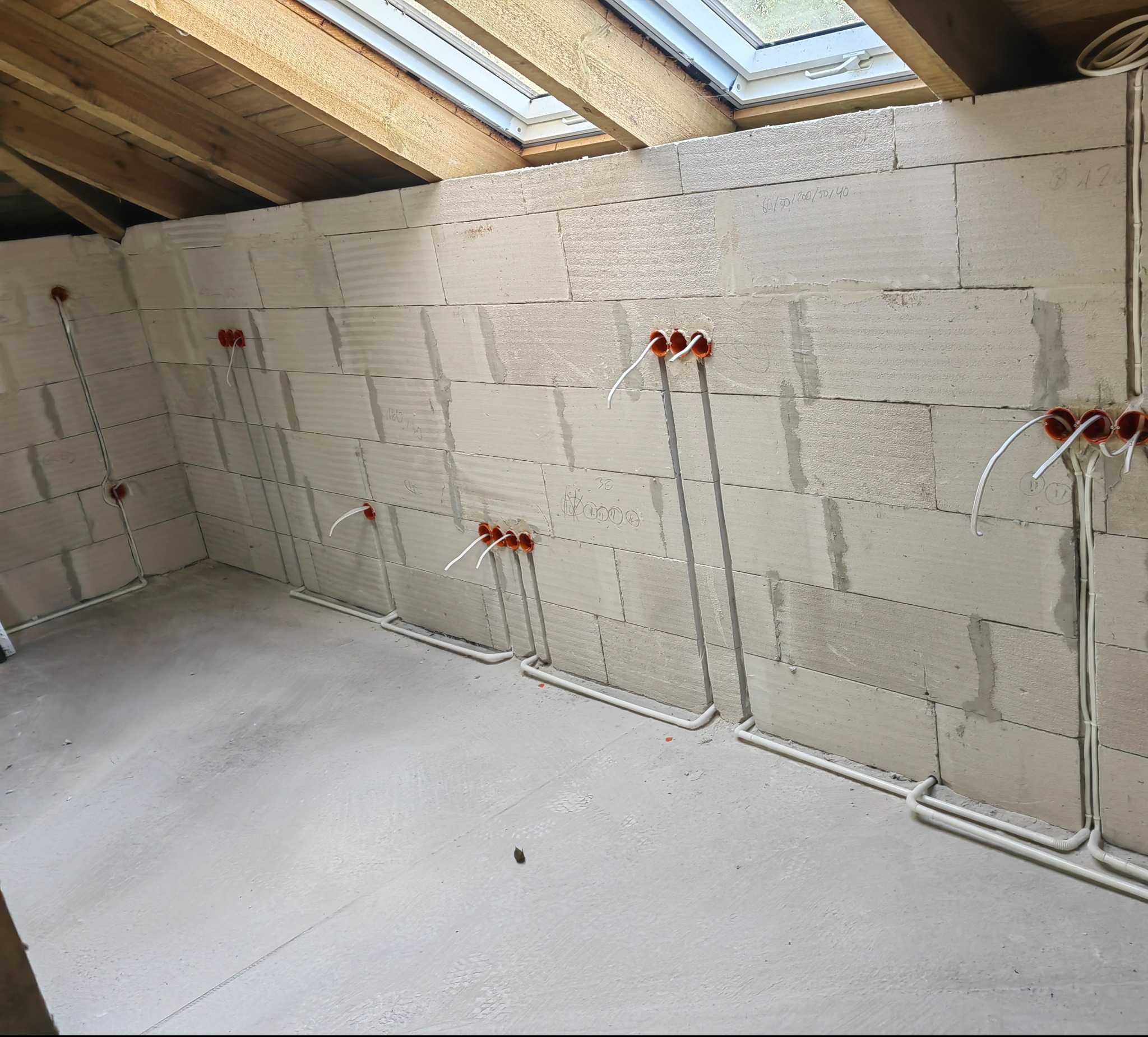 Surowy stan: Wnętrze w trakcie prac wykończeniowych, widoczne przewody elektryczne w peszlach prowadzone po ścianach z bloczków, puszki instalacyjne w kolorze pomarańczowym, sufit z drewnianych...