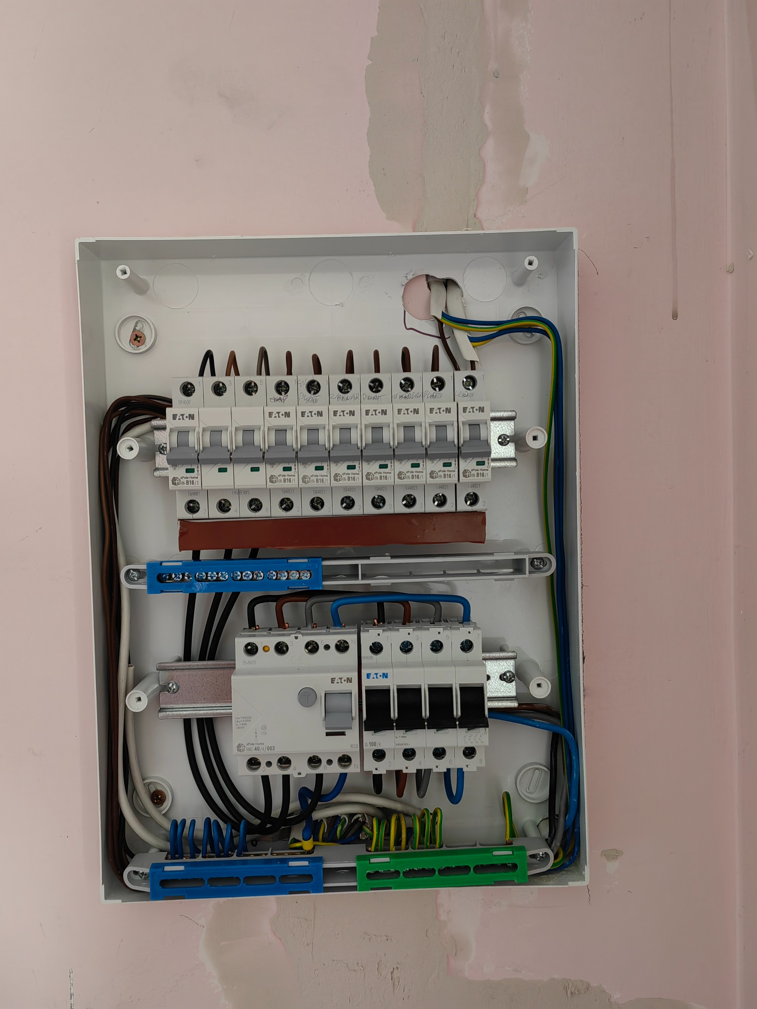 Otwarta skrzynka rozdzielcza Eaton z zamontowanymi bezpiecznikami i okablowaniem na różowej ścianie w trakcie montażu.