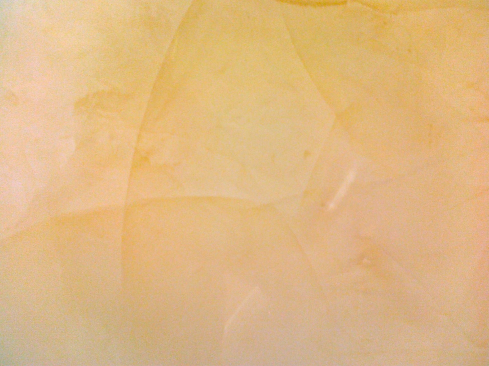 Delikatna, kremowo-żółta struktura ściany z subtelnymi, rozproszonymi smugami i nieregularnymi wzorami, przypominająca efekt dekoracyjnego tynku.