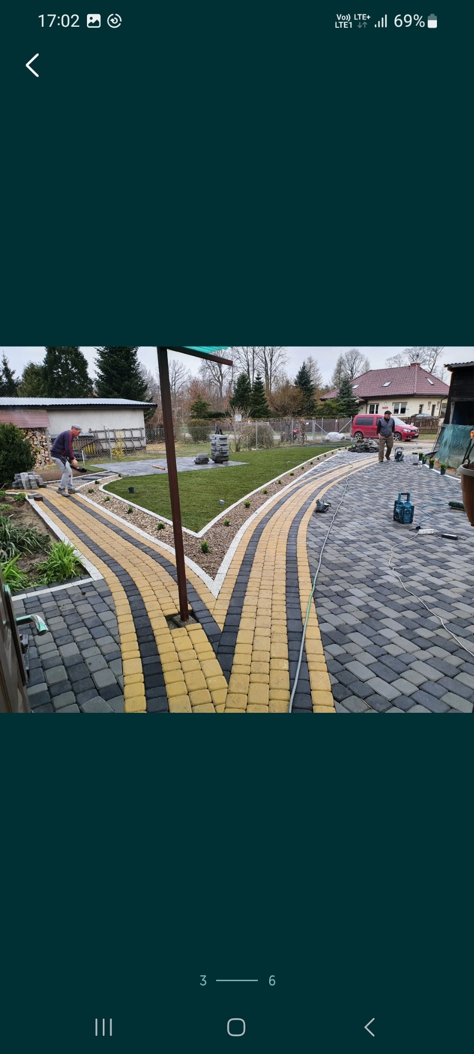 Świeżo ułożony chodnik z kostki brukowej w odcieniach szarości i żółci, rozwidlający się na dwie ścieżki, z widocznym pracownikiem i narzędziami w tle.