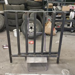 DON SERWIS Paweł Wójcik - Surowa, spawana konstrukcja metalowa, przypominająca fragment balustrady lub ogrodzenia, na tle opon samochodowych i warsztatowego nieładu.