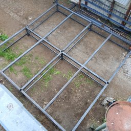 DON SERWIS Paweł Wójcik - Metalowa konstrukcja szkieletowa z profili, prawdopodobnie pod zabudowę, widziana z góry, na ziemi z fragmentami trawy i betonu.