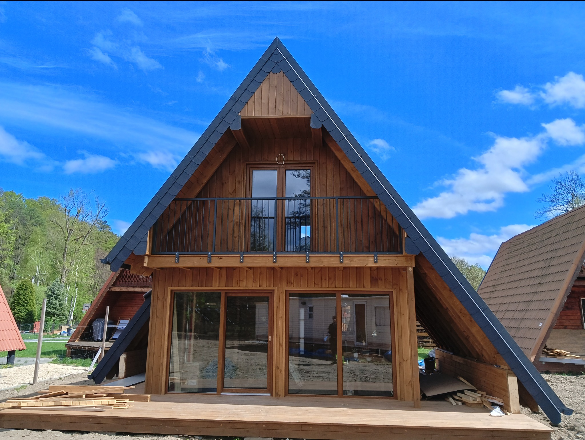 Nowoczesny, drewniany dom w stylu góralskim z balkonem i czarną balustradą na tle błękitnego nieba. Widoczne detale wykończenia dachu i drewniana elewacja.