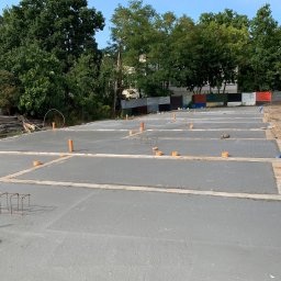 Zakład Budowlany Andrzej Korda - Zalane fundamenty z wystającymi rurami i zbrojeniami, przygotowane pod dalsze prace budowlane. Widoczne worki z cementem i otoczenie placu budowy.