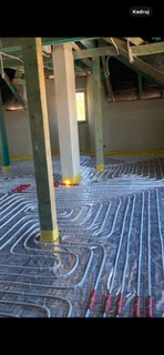 Montaż rur ogrzewania podłogowego na folii izolacyjnej w surowym wnętrzu poddasza z drewnianą konstrukcją stropu.