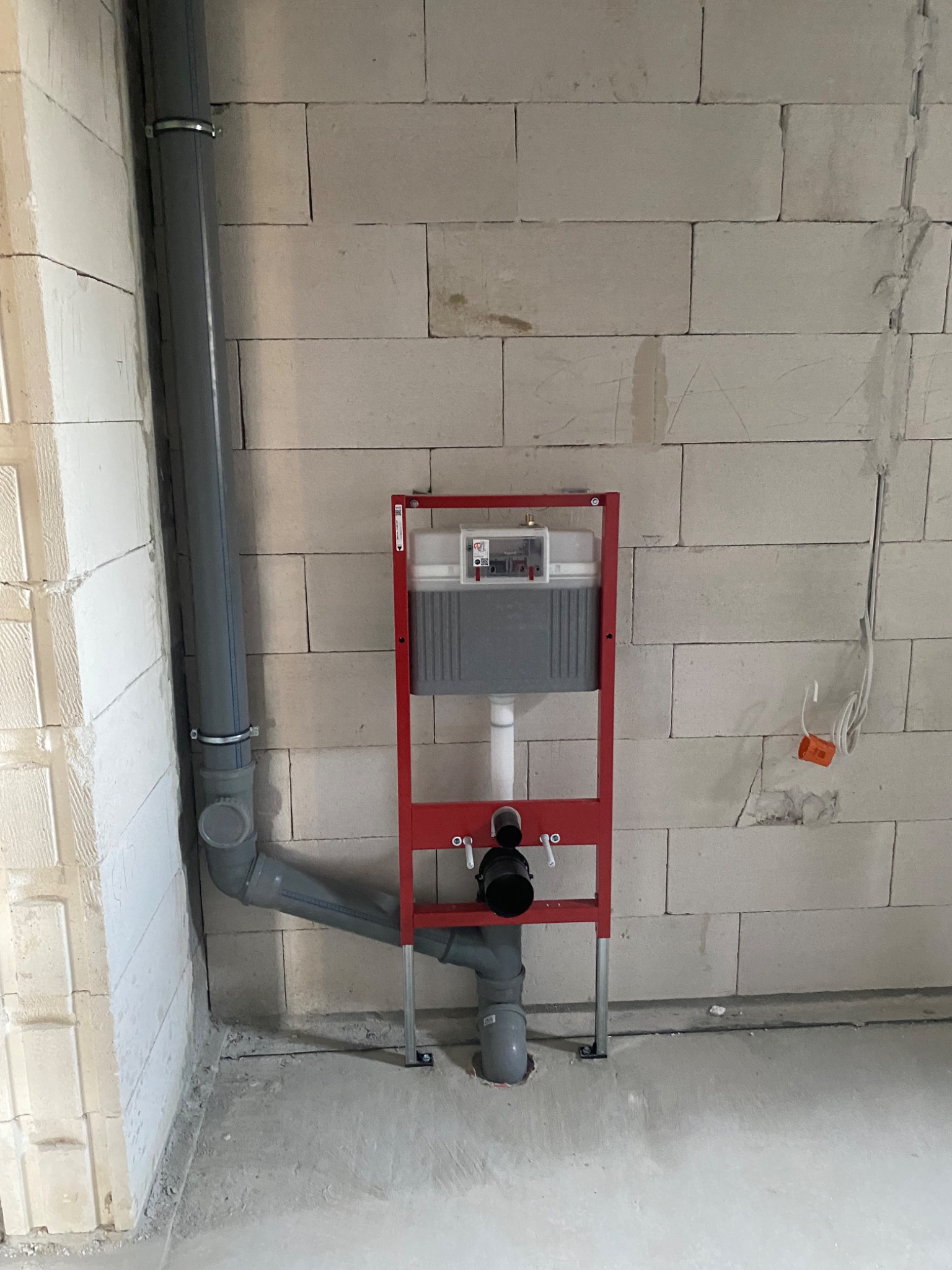 Stelaż podtynkowy WC z rurami odpływowymi zamontowany na surowej ścianie z betonu komórkowego.