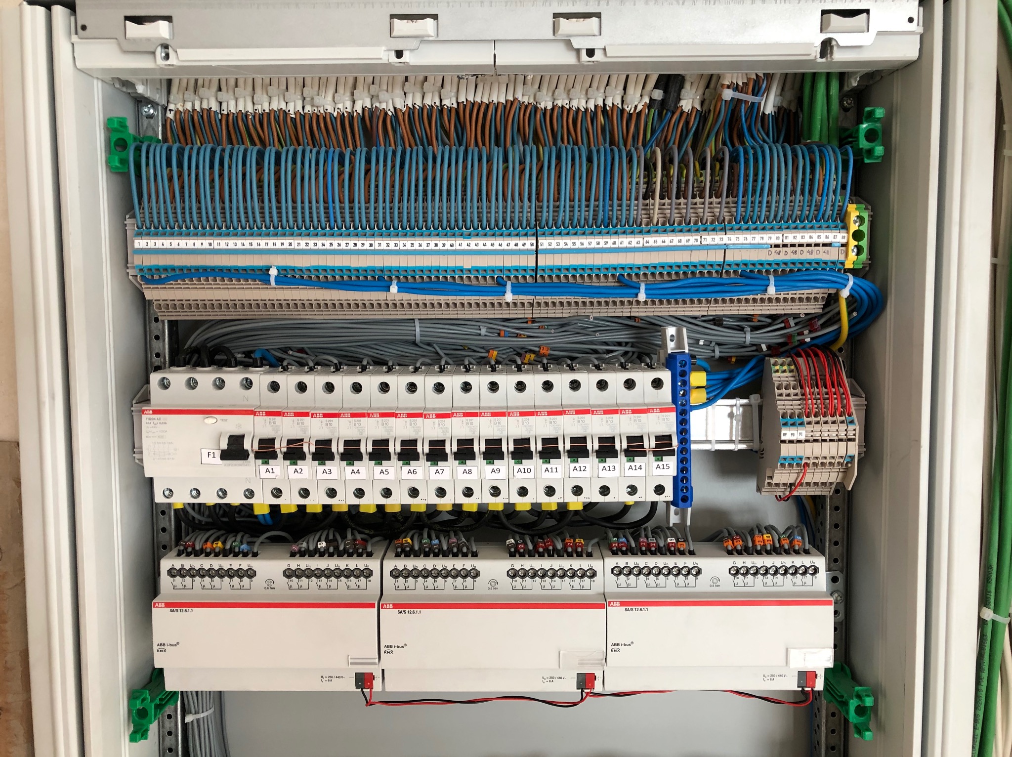 Otwarta szafa sterownicza z widocznymi bezpiecznikami, przekaźnikami i uporządkowanymi przewodami w różnych kolorach, ułożonymi w rzędach i oznaczonymi numerami.