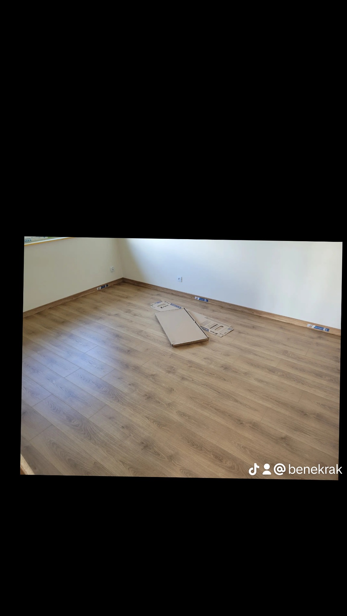 Pokój z nową podłogą z paneli w odcieniach brązu, widoczne listwy przypodłogowe i kartonowe opakowania po panelach, sugerujące świeżo zakończony montaż.