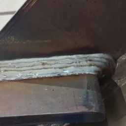 Szczegółowe zbliżenie spoiny łączącej dwie metalowe płyty pod kątem, widoczne nierówności i przebarwienia po procesie łączenia.