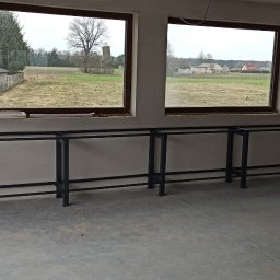 VIKTET-SPAV Viktor Slobodianiuk - Metalowa konstrukcja pod zabudowę kuchenną w surowym wnętrzu z dwoma oknami, przez które widać wiejski krajobraz. Elementy instalacji elektrycznej na ścianie.