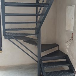 VIKTET-SPAV Viktor Slobodianiuk - Metalowe schody spiralne w surowym wnętrzu, z widocznymi przewodami elektrycznymi i skrzynką na ścianie. Schody pomalowane na ciemny kolor, z perforowanymi stopniami.