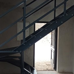 VIKTET-SPAV Viktor Slobodianiuk - Nowoczesne, metalowe schody z ażurowymi stopniami w surowym wnętrzu. Widoczne detale mocowań i spawów. W tle okno i otwarte drzwi.