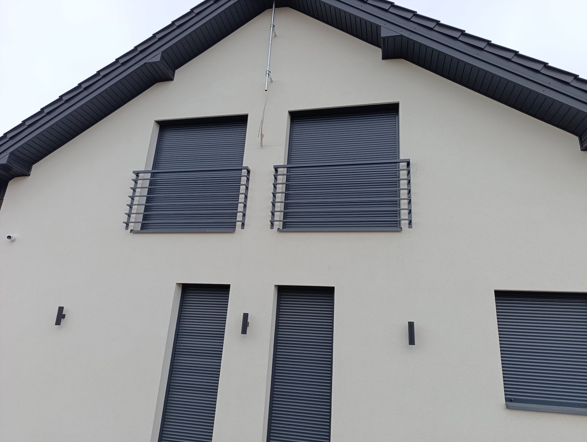 Elewacja domu z szarymi roletami zewnętrznymi i balkonami z metalowymi barierkami. Nowoczesne oświetlenie elewacyjne. Ujęcie z dołu.