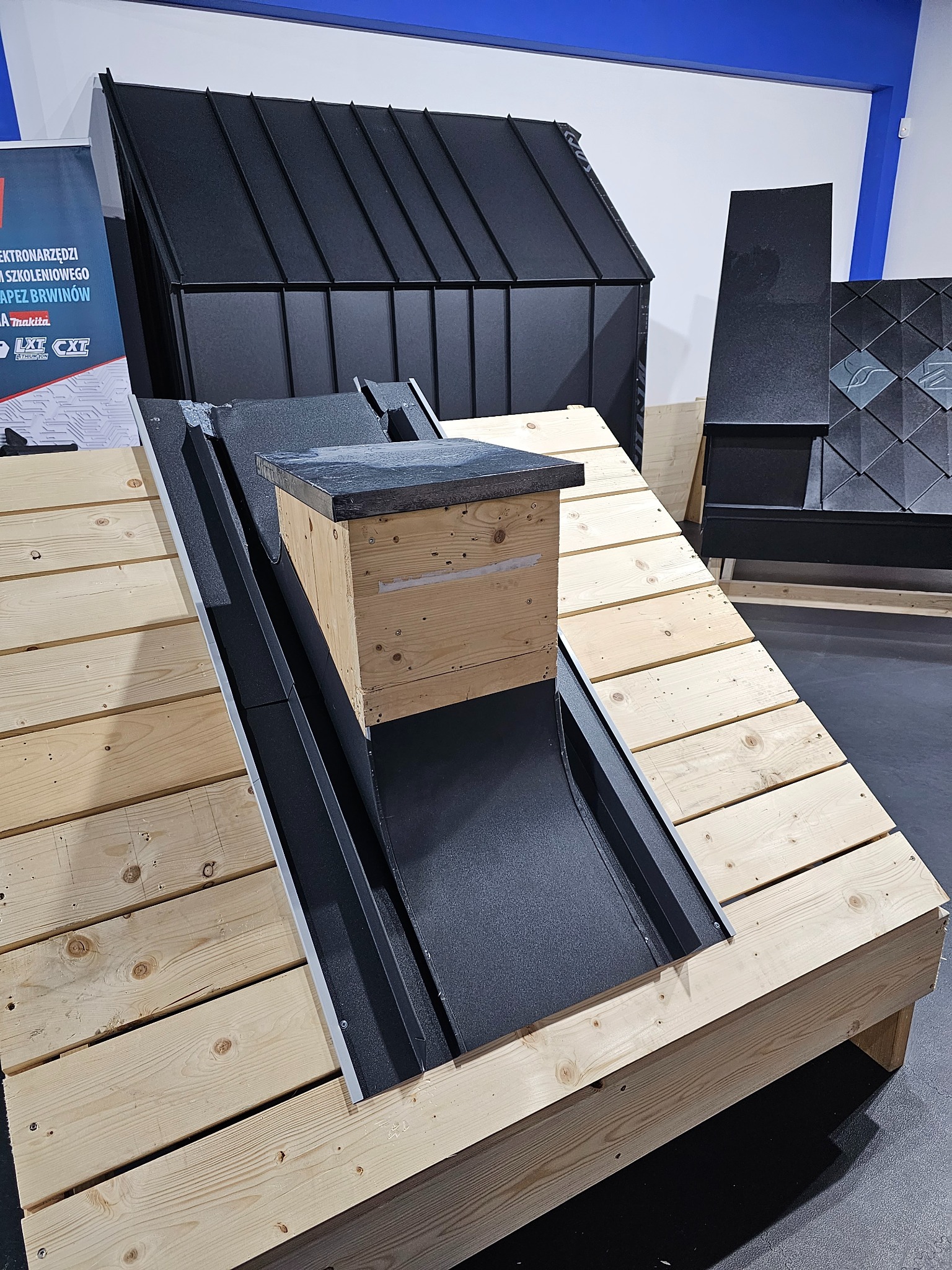 Ekspozycja przekroju dachu z obróbkami blacharskimi, drewnianą konstrukcją i elementami krycia, prezentowana na stoisku targowym.