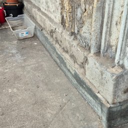 J.R.INVEST HOUSE JAN RATAJCZAK - Fragment balkonu z odpadającą farbą i widocznymi uszkodzeniami tynku, obok leżą doniczki i plastikowy pojemnik.