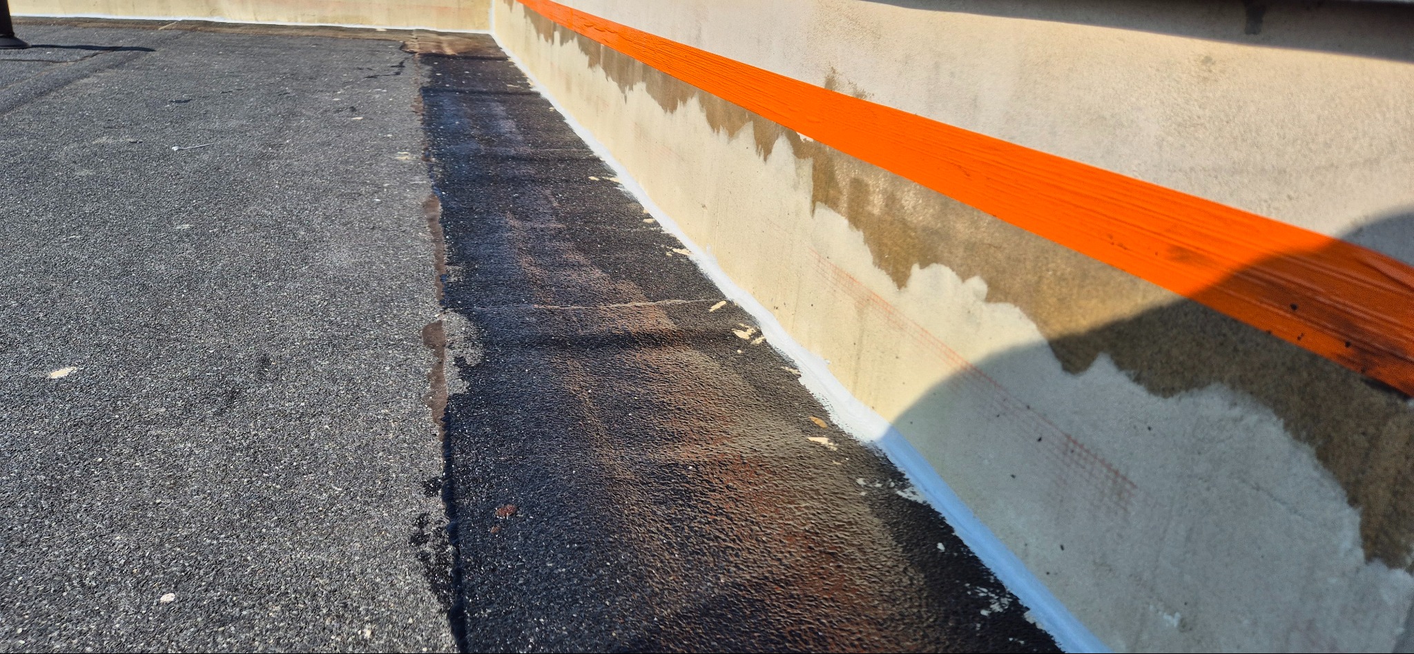 Wykończona powierzchnia dachu z papy po naprawie, z widocznym uszczelnieniem przy ścianie i pomalowanym na pomarańczowo pasem na elewacji.