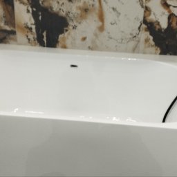 Yakiv Shevchenko - Nowoczesna, biała wanna wolnostojąca z czarną armaturą na tle ściany wyłożonej płytkami imitującymi marmur w odcieniach brązu i beżu. Minimalistyczny design.