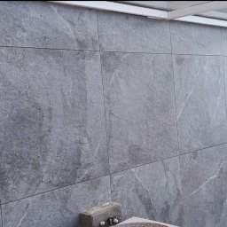 Yakiv Shevchenko - Szara, marmurkowa okładzina ścienna z widocznymi fugami, tworząca nowoczesny design. Fragment balkonu z widocznym otoczeniem zewnętrznym.