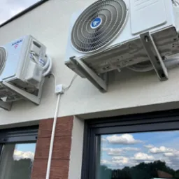 Dwa agregaty klimatyzacyjne marki Kaisai zamontowane na elewacji budynku z widocznymi oknami i elementami dekoracyjnymi z imitacji drewna.