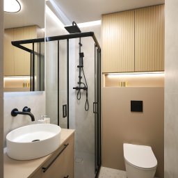 JAVA Architekci - Nowoczesna łazienka z kabiną prysznicową typu walk-in z czarnymi ramami, owalną białą umywalką nablatową z czarną armaturą, podświetlanymi szafkami z lamelami i wiszącą toaletą.