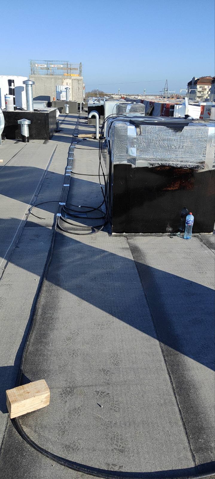 Instalacja przewodów na dachu budynku w Żyrardowie. Widoczne kable w korytkach, zabezpieczone taśmą, oraz urządzenia klimatyzacyjne. Ujęcie z góry, w słoneczny dzień.