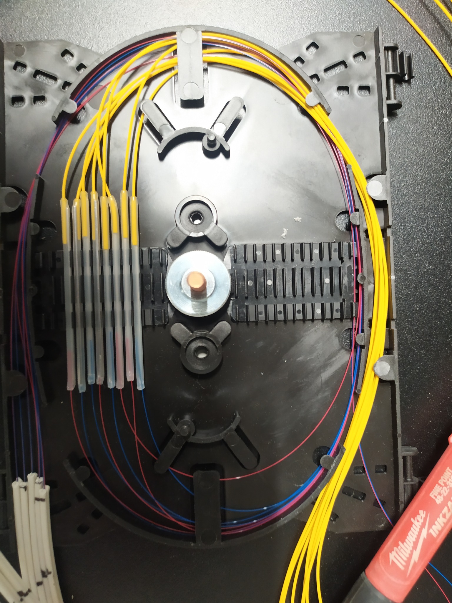 Rozdzielnica światłowodowa z precyzyjnie ułożonymi kablami w kolorach żółtym, czerwonym i niebieskim. Widoczny marker Milwaukee. Detal instalacji.