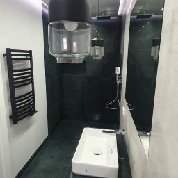 RAD-BUD Radosław Czubasiewicz - Nowoczesna łazienka z czarnymi płytkami, podwieszaną umywalką na szafce w kolorze petrol blue, dużym lustrem i designerskimi lampami wiszącymi z przezroczystymi kloszami.